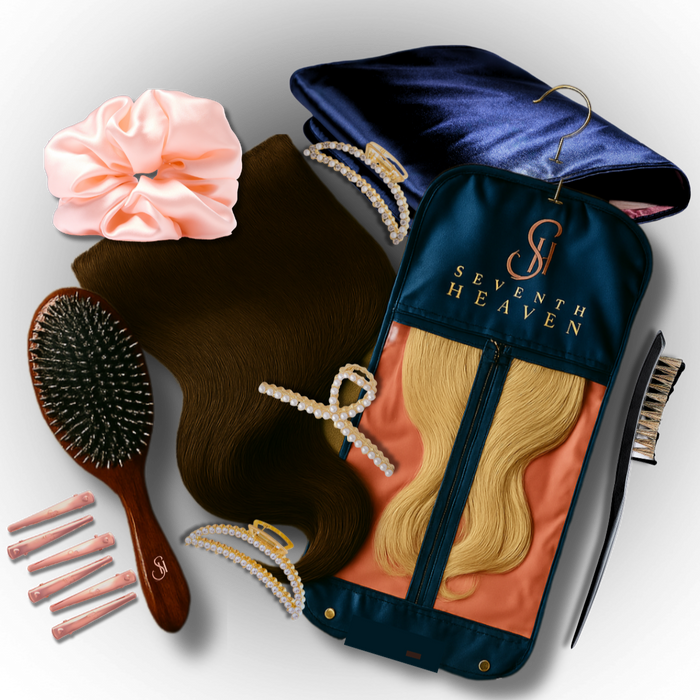 Flat lay of Seventh Heaven clip-in hair extensions deluxe bundle, including brunette and blonde extensions, luxury hanger bag, silk scrunchies, pearl clips, sectioning comb, and boar bristle brush