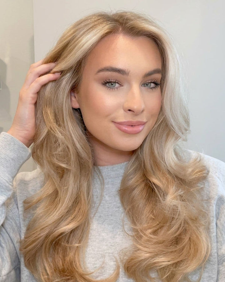Blonde woman checking her scalp and hair while wearing clip-in hair extensions, demonstrating proper application and healthy hair care.