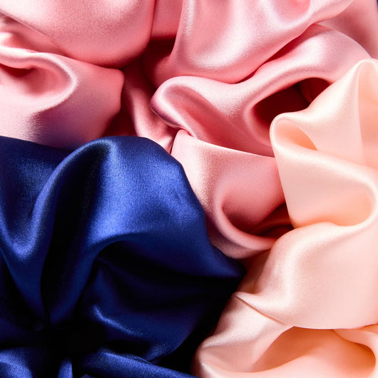 Close-up of luxury mulberry silk scrunchies in blush pink, navy blue, and soft peach, featuring smooth satin texture designed to reduce hair breakage and creasing